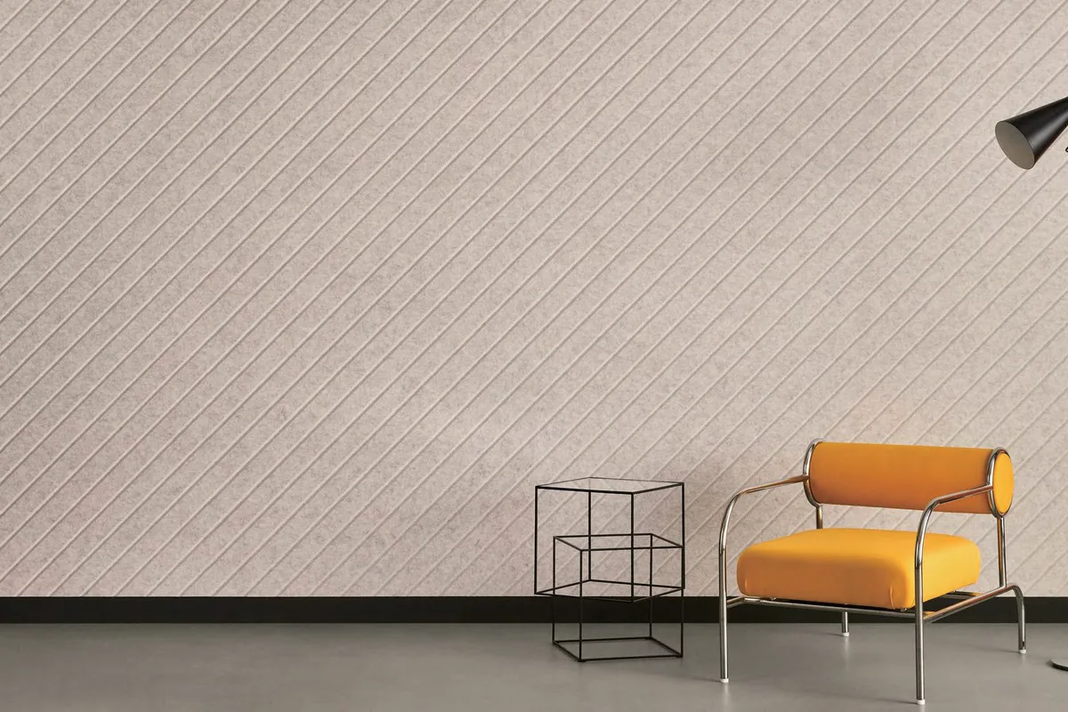 Wand aus diagonal gravierten Akustikpaneelen hinter einem orangefarbenen Sessel